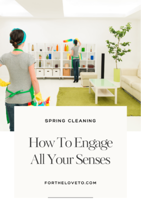 A woman wearing cleaning gloves and an apron tidies up a bright, modern living room with white shelves and green decor during spring cleaning