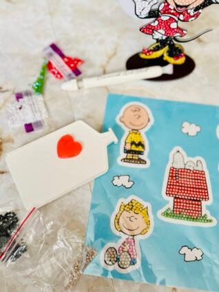 Peanuts-themed diamond painting stickers featuring Charlie Brown and Snoopy partially completed on a craft table