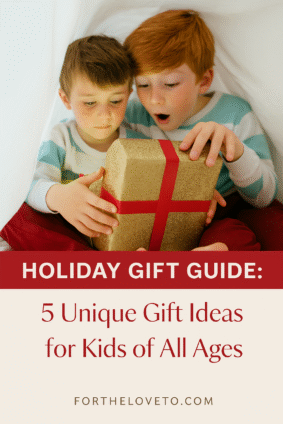 Two brothers in cozy pajamas sitting under a white blanket fort, surprised while opening a glittery gold present with a red ribbon. Overlay text reads 'Holiday Gift Guide: 5 Unique Gift Ideas for Kids of All Ages' with fortheloveto.com branding.