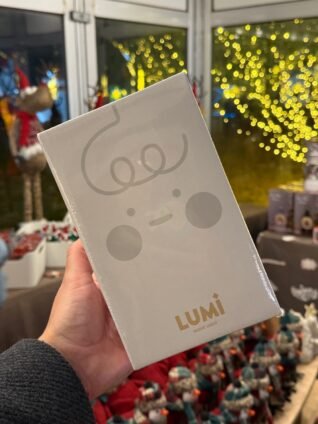 Close-up of a Lumi night light souvenir held inside the LuminoCity gift shop with glowing holiday decor in the background.
