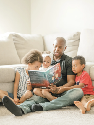 Father reading a children’s book with his kids at home to encourage reading over the holiday break