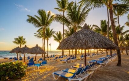 Romantic fall getaway in Punta Cana with palm trees, beach chairs, and thatched umbrellas at sunset.