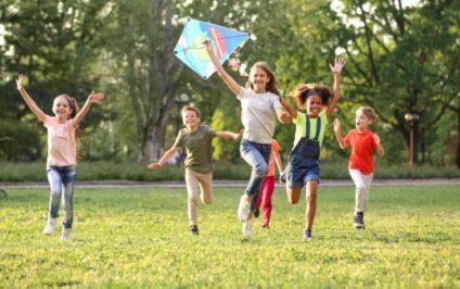 Creating inclusive environments where every child can thrive as a diverse group of children run and play together outdoors with a colorful kite.