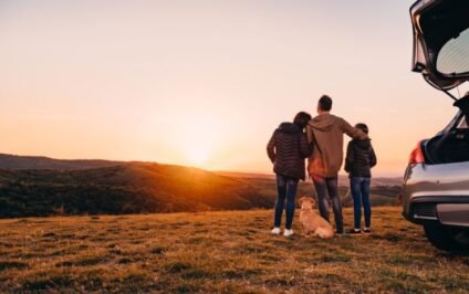 Family and dog watching the sunset beside their car during a multi-state road trip.