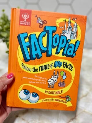 Hand holding FACTopia!, a brightly illustrated children’s book featuring a trail of 400 connected facts.
