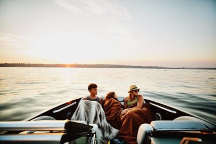 Family relaxing under blankets on a boat at sunset, illustrating a coastal boat care guide.