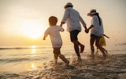 Family holding hands while running through shallow water at sunset.